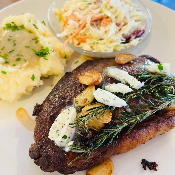 A steak with garlic, rosemary, and herb butter, served with mashed potatoes and coleslaw.