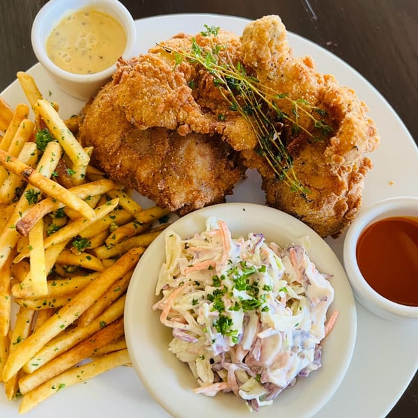 Crispy fried chicken with french fries, coleslaw, and two dipping sauces on a white plate.