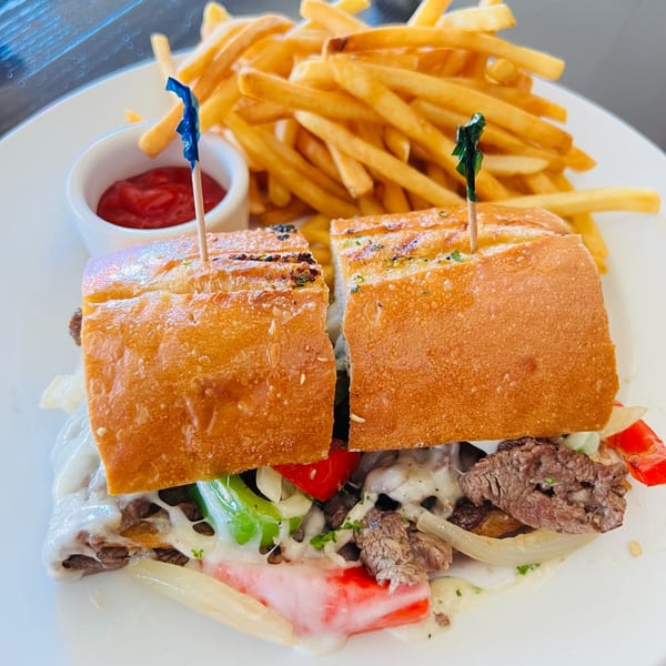 A steak and cheese sub with peppers and onions, served with a side of fries and ketchup.