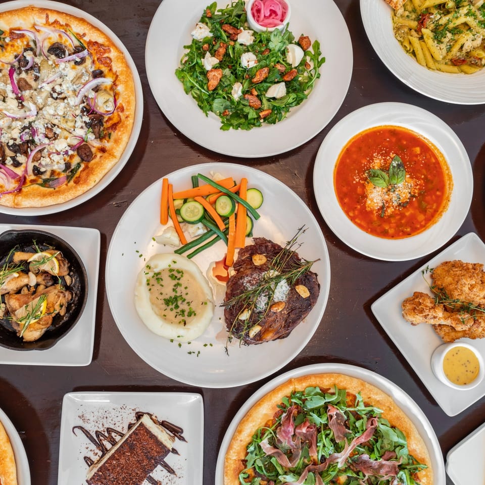 Overhead view of various Red Rooster Brick Oven dishes, including pizzas, pasta, steak, and dessert.