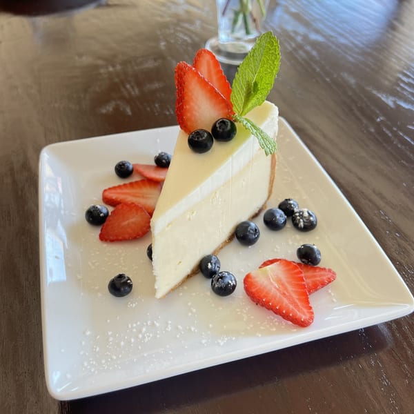 A slice of cheesecake topped with strawberries, blueberries, and mint on a white plate.