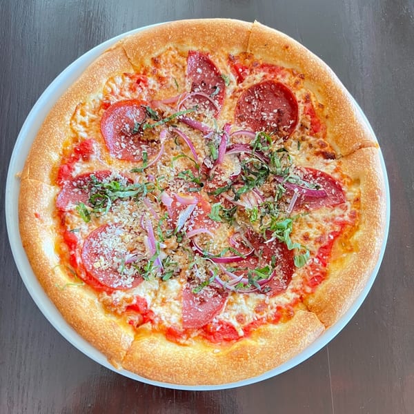Red Rooster Brick Oven pepperoni pizza with red onions, basil, and parmesan on a white plate.