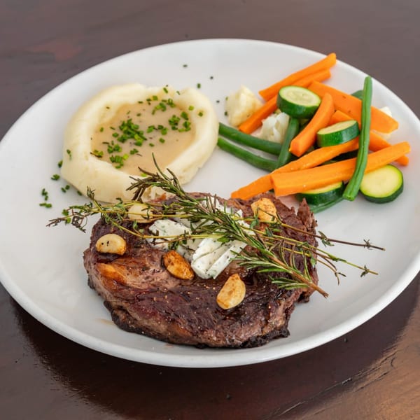 Grilled steak with garlic, herbs, mashed potatoes with gravy, and mixed vegetables on a white plate.