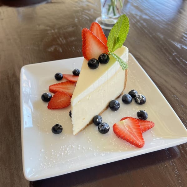 Slice of cheesecake with strawberries, blueberries, and mint on a white plate.